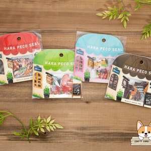 May include: Four colourful sticker sheets with a shop theme. Each sheet features a different coloured awning and a variety of stickers, including a shop sign, a door, and a window. The text on the sheets reads "HARA PECO SEAL" and "EAGLE JAPAN INC."