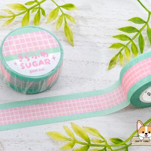 Pode incluir: Um rolo de fita washi com um padr&atilde;o quadriculado rosa e verde. A fita tem as palavras "Sugar BGM Inc." impressas nela.