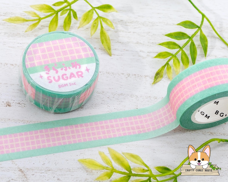 Pode incluir: Um rolo de fita washi com um padr&atilde;o quadriculado rosa e verde. A fita tem as palavras "Sugar BGM Inc." impressas nela.