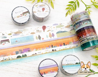 May include: Assortment of colorful washi tapes with Japanese text and illustrations of cityscapes, clouds, and buildings. The tapes are rolled up and displayed on a white wooden surface.