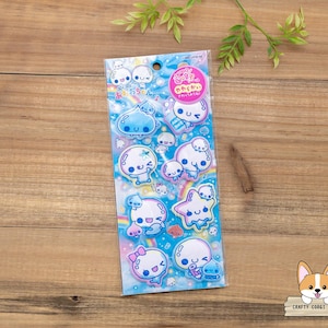 May include: A package of stickers featuring cute, cartoonish characters in various poses. The stickers have a blue and pink color scheme with a rainbow and star design. The package has Japanese text and a pink circular sticker.