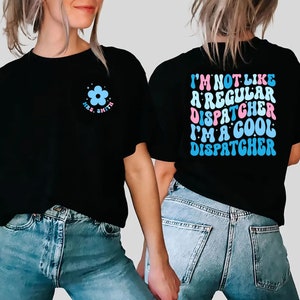 May include: Two black t-shirts with a retro font design. One shirt has a blue flower with the text "Mrs. Smith" on the front. The other shirt has the text "I'm not like a regular dispatcher I'm a cool dispatcher" on the back.