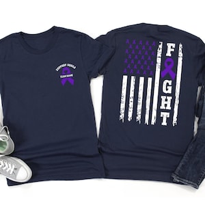 Puede incluir: Camisetas azul marino con gráficos de lazo morado. Una camiseta tiene el texto "SUPPORT SQUAD" y "TEAM NAME", la otra un diseño de bandera americana desgastada con la palabra "FIGHT".