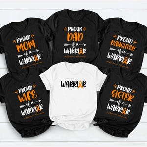 May include: A collection of six t-shirts for leukemia awareness. Five black shirts feature white and orange text reading Proud Mom, Dad, Daughter, Wife, and Sister of a Warrior with an orange ribbon. One white shirt reads Warrior.