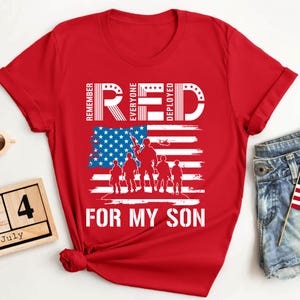 Könnte beinhalten: Rotes T-Shirt mit patriotischem Design. Das Shirt zeigt den Text "RED" mit den Worten "Remember Everyone Deployed" und "For My Son". Eine amerikanische Flagge und Silhouetten von Soldaten sind ebenfalls enthalten.