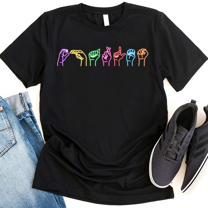 Op de afbeelding: Zwart T-shirt met een afbeelding van regenboogkleurige handen die het woord "familie" in Amerikaanse Gebarentaal tekenen.