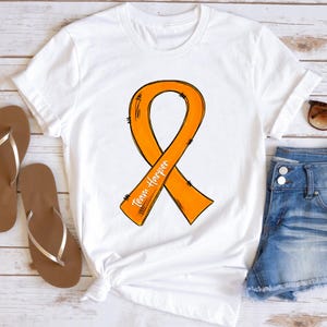 Può includere: T-shirt bianca con un nastro arancione di sensibilizzazione e la scritta "Team Harper". Il nastro è un simbolo di sostegno. La maglietta è in stile casual, adatta all'uso quotidiano.