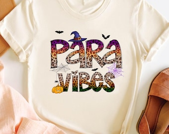 May include: A white t-shirt with a colorful graphic print that says "Para Vibes". The graphic features a witch's hat, bats, and spiderwebs in a leopard print pattern.