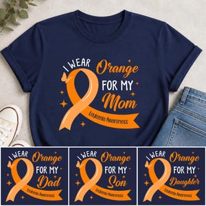Könnte beinhalten: Ein dunkelblaues T-Shirt mit kurzen Ärmeln und einem Grafikdesign, das ein orangefarbenes Awareness-Band, einen kleinen Schmetterling und den Text I WEAR Orange FOR MY Mom LEUKEMIA AWARENESS sowie kleine weiße und orangefarbene Sterne zeigt.