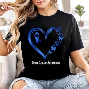 May include: Black t-shirt featuring a blue heart with a ribbon and butterflies, with the text "Colon Cancer Awareness". The design is centered on the shirt. The shirt is made of a soft material.