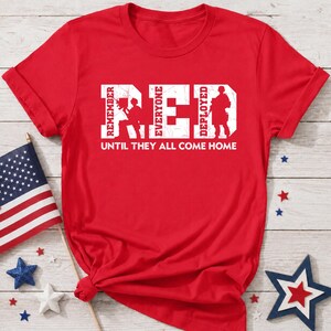Könnte beinhalten: Ein leuchtend rotes Kurzarm-T-Shirt mit dem weißen, abgenutzten Schriftzug R.E.D., in dessen Buchstaben Silhouetten von Soldaten zu sehen sind. Darunter steht der Text REMEMBER EVERYONE DEPLOYED UNTIL THEY ALL COME HOME.
