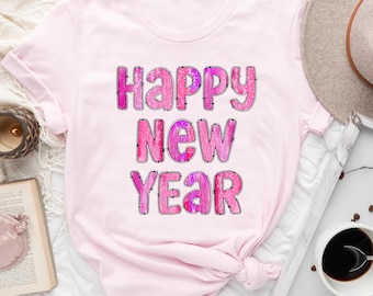 May include: Pink t-shirt with the text "Happy New Year" in a pink and white glittery font.