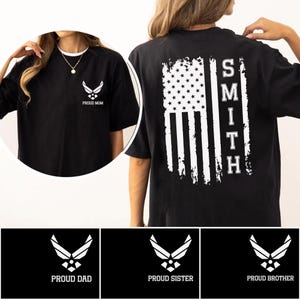 May include: Black t-shirts with white graphics. One shirt features the Air Force emblem and the text "PROUD MOM". Another displays a distressed American flag design with the name "SMITH". Additional shirts say "PROUD DAD", "PROUD SISTER", and "PROUD BROTHER".