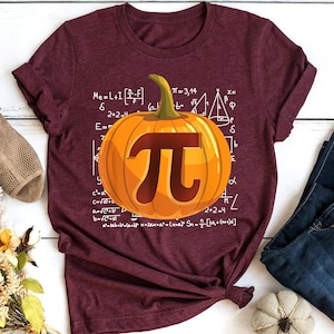 May include: A maroon t-shirt with a white pumpkin design featuring the mathematical symbol pi. The pumpkin is surrounded by mathematical equations and formulas.