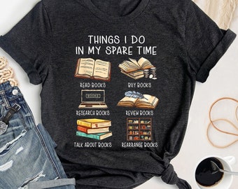 May include: A dark grey t-shirt with the text "Things I do in my spare time" and illustrations of books. The illustrations depict reading, buying, researching, reviewing, talking about, and rearranging books.