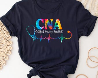 May include: A navy blue t-shirt with a rainbow tie-dye design. The shirt features the text "CNA Certified Nursing Assistant" and a stethoscope with a heartbeat graphic.