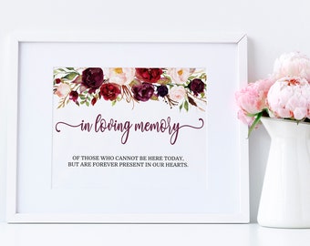May include: A white framed print with a floral design in shades of burgundy, pink, and green. The text "in loving memory" is written in a cursive font. The text below reads "Of those who cannot be here today, but are forever present in our hearts."