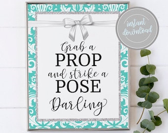 May include: A teal and silver printable sign with a white bow and the text "Grab a PROP and strike a POSE Darling".