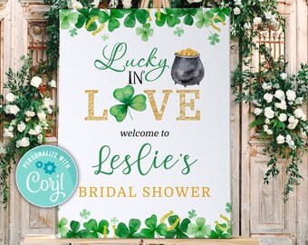 Könnte beinhalten: Ein weißes Schild mit grünen Kleeblättern und goldenem Glitzer lautet "Lucky in Love" und "Willkommen zu Leslies Bridal Shower". Ein Topf mit Gold befindet sich über dem Text.