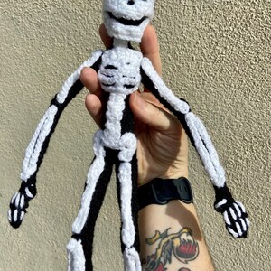 May include: A crocheted skeleton doll with black and white yarn. The skeleton is smiling and has a friendly expression.