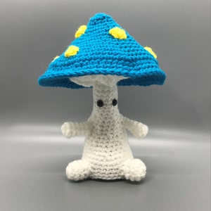 May include: A crocheted mushroom plush toy with a blue cap and yellow spots. The mushroom has a white body with black eyes.