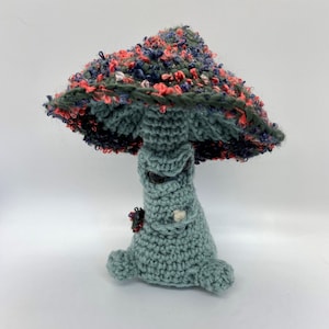 May include: A crocheted mushroom toy with a green body and a multi-colored cap. The cap is made of yarn with red, blue, and white accents.