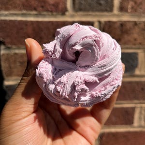 Puede incluir: Un montón de slime texturizado de color rosa claro con una consistencia espesa y batida. La sustancia presenta remolinos y crestas visibles en toda su superficie, creando una apariencia densa y mate que mantiene su forma al sostenerla.