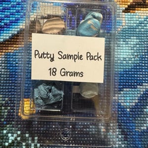 May include: A clear plastic container holding a putty sample pack. The label reads "Putty Sample Pack 18 Grams." Inside are samples of putty in various colors, including tan, blue, and gray. The container is on a textured, multi-colored surface.
