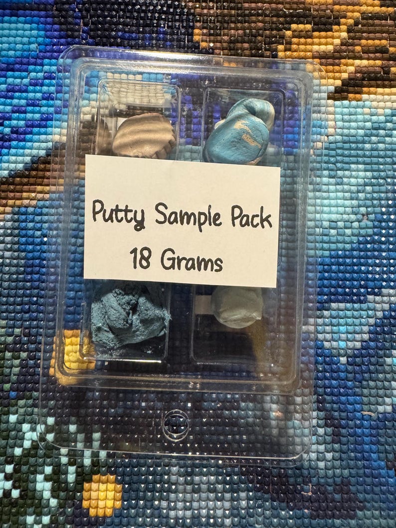 May include: A clear plastic container holding a putty sample pack. The label reads "Putty Sample Pack 18 Grams." Inside are samples of putty in various colors, including tan, blue, and gray. The container is on a textured, multi-colored surface.