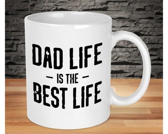 Op de afbeelding: Witte keramische koffiemok met zwarte tekst die "Dad Life - Is The - Best Life" luidt.