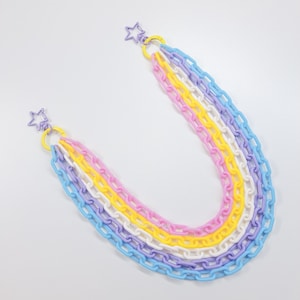 May include: A colorful chain necklace featuring a rainbow of pastel colors: light blue, lavender, white, yellow, and pink. The necklace has star-shaped clasps and is made of plastic. The chain links are uniform in size and shape.