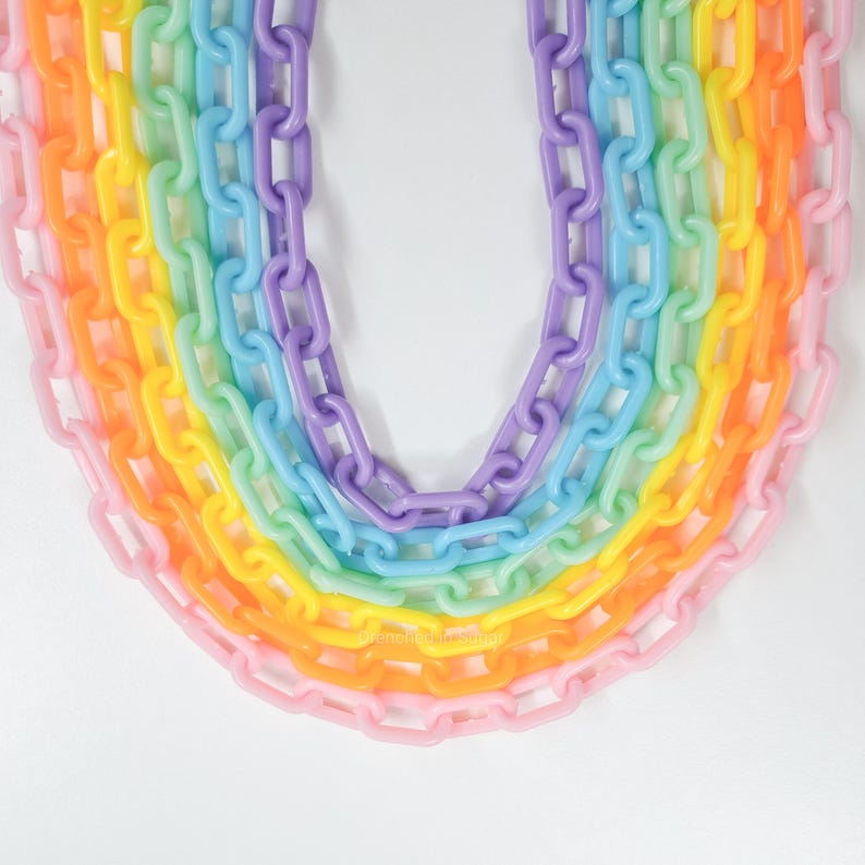 May include: A rainbow chain made of plastic links. The chain is made up of seven different colors: pink, orange, yellow, green, blue, indigo, and violet.
