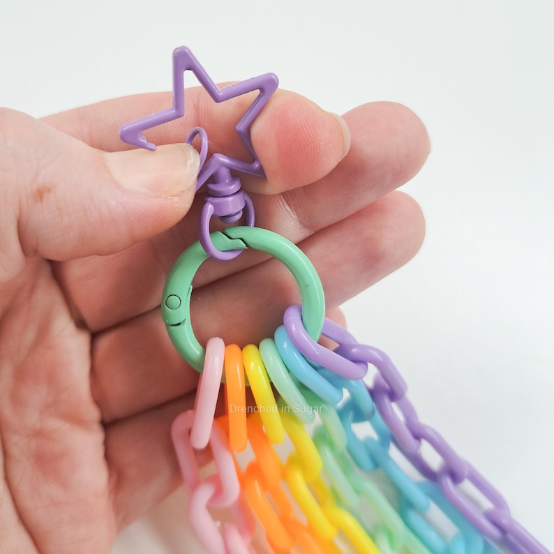 May include: A rainbow colored chain with a purple star charm and a green metal clasp. The chain is made of plastic and is perfect for adding a pop of color to any bag or keychain.