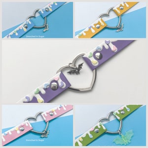 Puede incluir: Cinco variaciones de color diferentes de un collar de cuero blanco con un dije de corazón plateado y un dije de murciélago. El collar tiene un diseño de caramelo que gotea con corazones de color pastel. El texto "Drenched in Sugar" es visible en dos de los collares.
