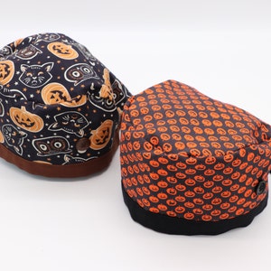 May include: Two Halloween themed surgical scrub hats. One hat features a black background with orange pumpkins and black cats. The other hat features a black background with orange pumpkins.