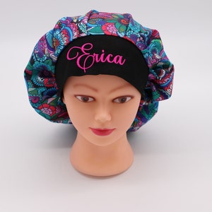 Könnte beinhalten: Eine schwarze OP-Mütze mit einem bunten Paisley-Muster und dem Namen "Erica" in Pink auf der Vorderseite bestickt.