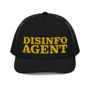 May include: Black trucker hat with a mesh back and a curved brim. The front of the hat features the embroidered text "DISINFO AGENT" in a bold, yellow font. A stylish accessory for everyday wear.