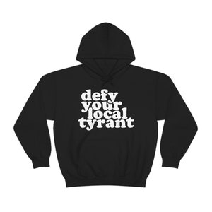 May include: Black hooded sweatshirt with the white text "defy your local tyrant". The hoodie has a drawstring and a front pocket. The text is in a bold, rounded font.