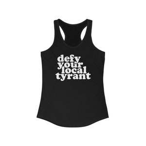 May include: Black racerback tank top with the white text "defy your local tyrant". The tank top has a scoop neck and a racerback design. The text is in a bold, sans-serif font.