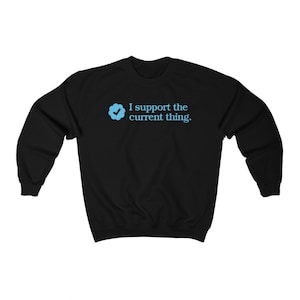 Könnte beinhalten: Schwarzer Pullover mit einem blauen Häkchen-Symbol und dem Text "Ich unterstütze das Aktuelle."