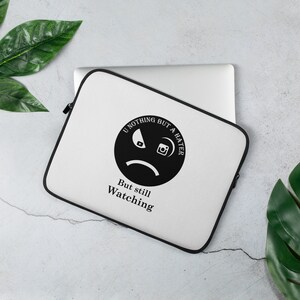 May include: White laptop sleeve with a black zipper and trim. The sleeve features a black graphic of a sad face with the text "U NOTHING BUT A HATER" and "But still Watching". The sleeve is on top of a silver laptop.