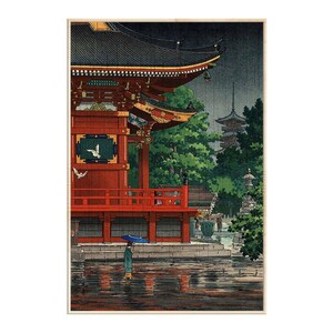 May include: A framed art print depicting a traditional red temple structure during a rainstorm. A figure holding a blue umbrella stands in the foreground near a reflective pool of water. Green trees and a distant pagoda are visible in the background.