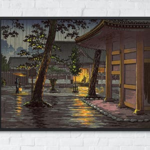 May include: A framed art print depicting a rainy evening scene at a Japanese temple complex. The image features a wooden structure with glowing yellow light, tall trees, and a person holding a yellow umbrella walking through the wet courtyard.
