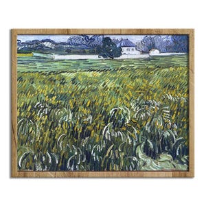 May include: A framed print of a landscape painting. The artwork depicts a field of tall grass in shades of green and yellow, with a white building and trees in the background. The frame is made of light brown wood.