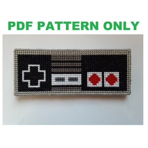 May include: A handmade, cross-stitched controller design in black, gray, white, and red. The controller features a directional pad, buttons, and a rectangular shape. The text "PDF PATTERN ONLY" is in green at the top.