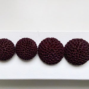May include: Four dark purple round buttons with a textured surface. The buttons are arranged in a row on a white background.