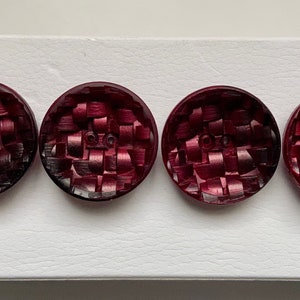 Peut inclure: Quatre boutons ronds de couleur rouge foncé avec un motif tissé. Les boutons ont une finition brillante.