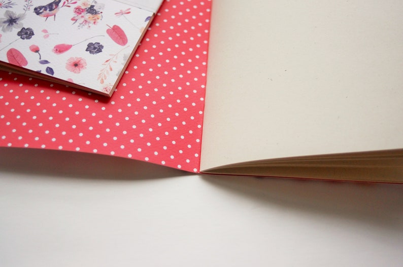 Może przedstawiać: R&oacute;żowy notes z białymi kropkami na okładce. Notes jest otwarty, ukazując puste białe strony.