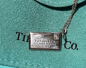 May include: A silver necklace with a pendant that says "Tiffany & Co. 727 Fifth Avenue New York, NY 10022" on a turquoise blue velvet pouch.