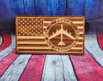 May include: Wooden sign with an American flag design and a circle with the text "Peace the old fashioned way" and a silhouette of a B-52 bomber inside the circle.